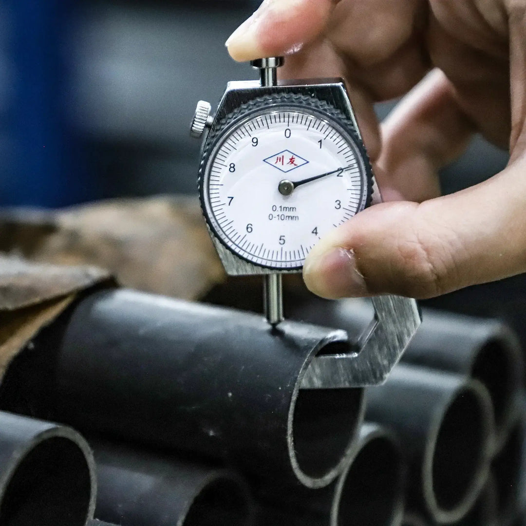 Close-up of a hand using a micrometer to measure the thickness of metal pipes.